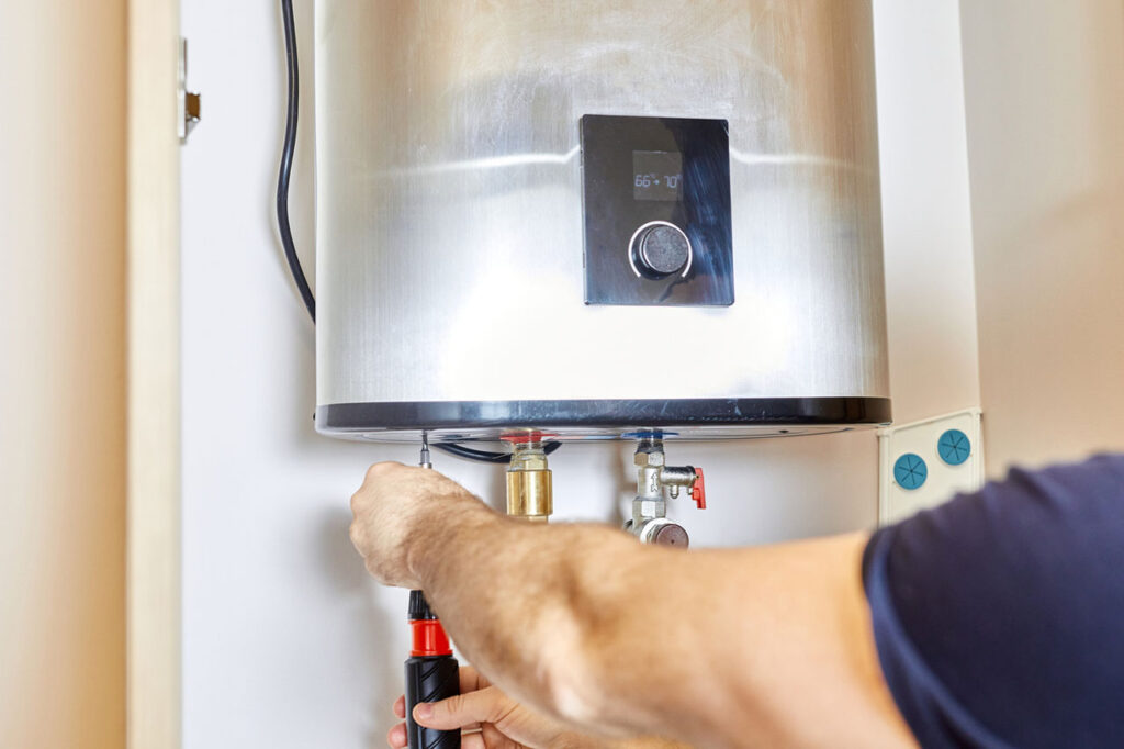 A plumber using a screwdriver to service a wall-mounted water heater with a digital display, showcasing professional maintenance.