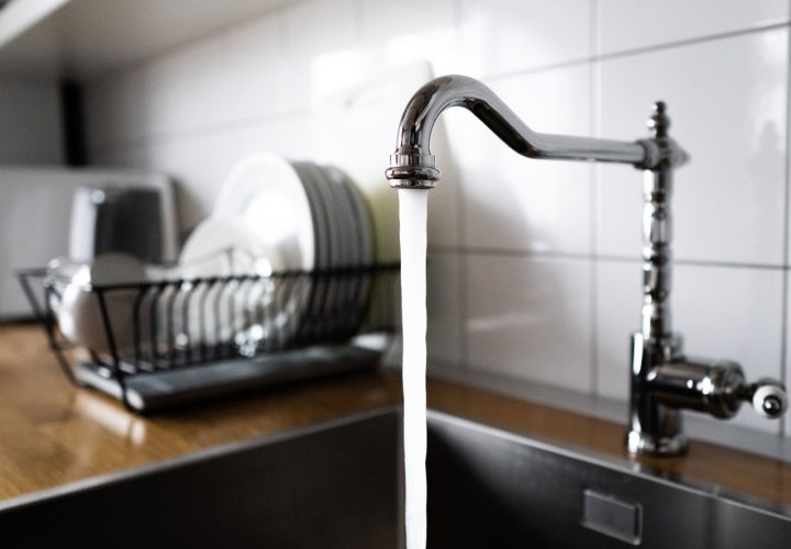 Close-up of water flowing from a modern kitchen faucet with dishes in the background, demonstrating everyday kitchen plumbing efficiency.
