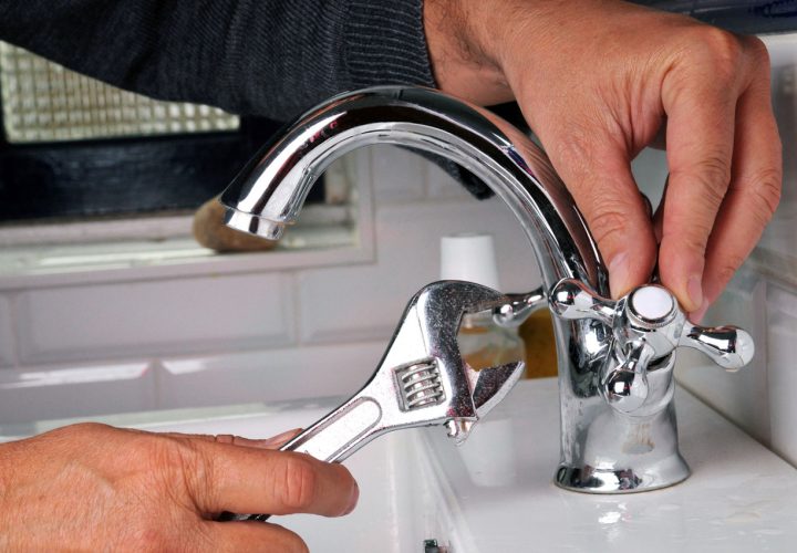 Close-up of a plumber's hands adjusting a shiny chrome kitchen faucet with a wrench, focusing on routine maintenance.